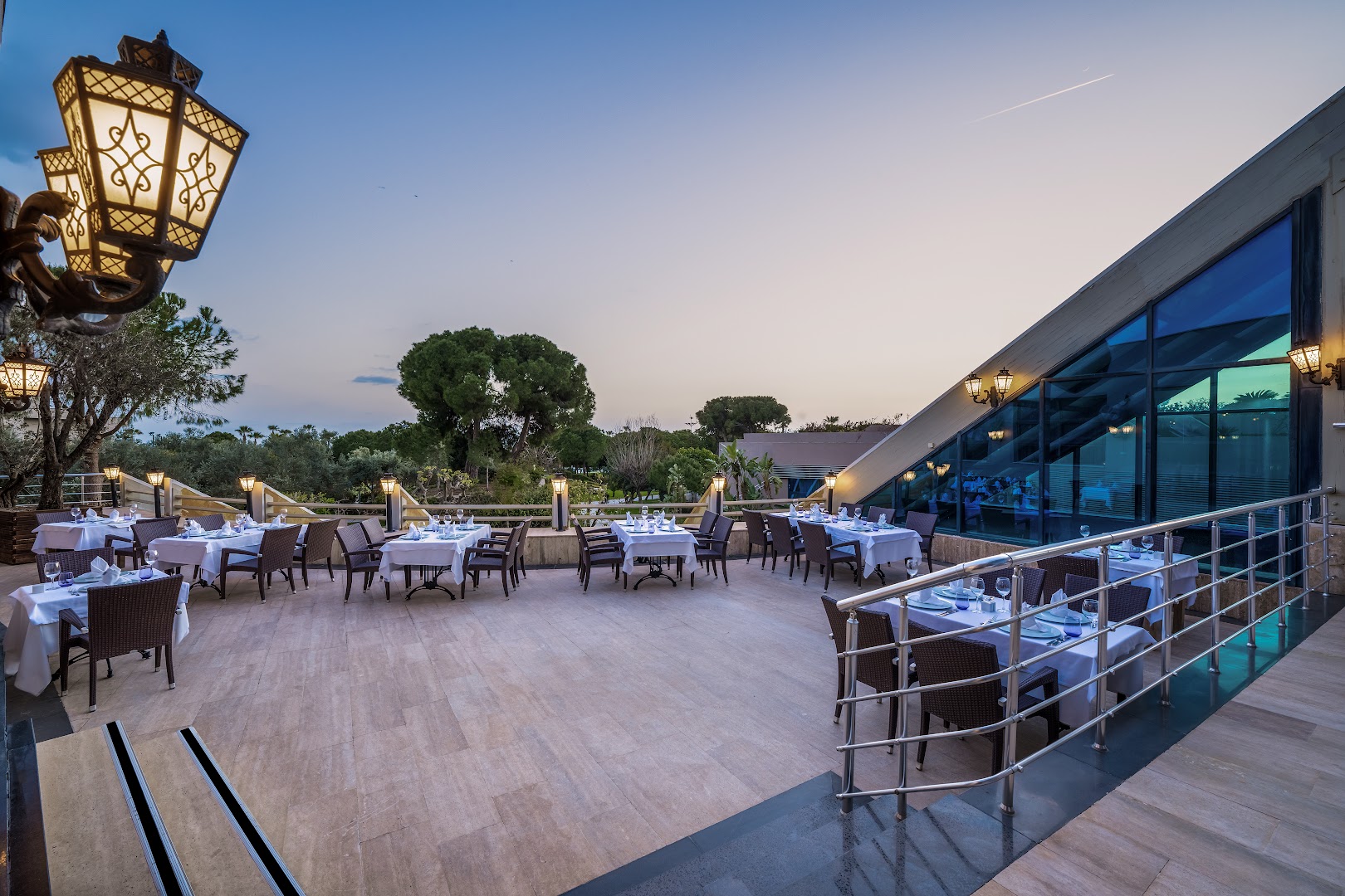 Susesi Luxury Resort restorāna āra terase ar klātiem galdiem un dekoratīvām laternām vakara krēslā Belekā