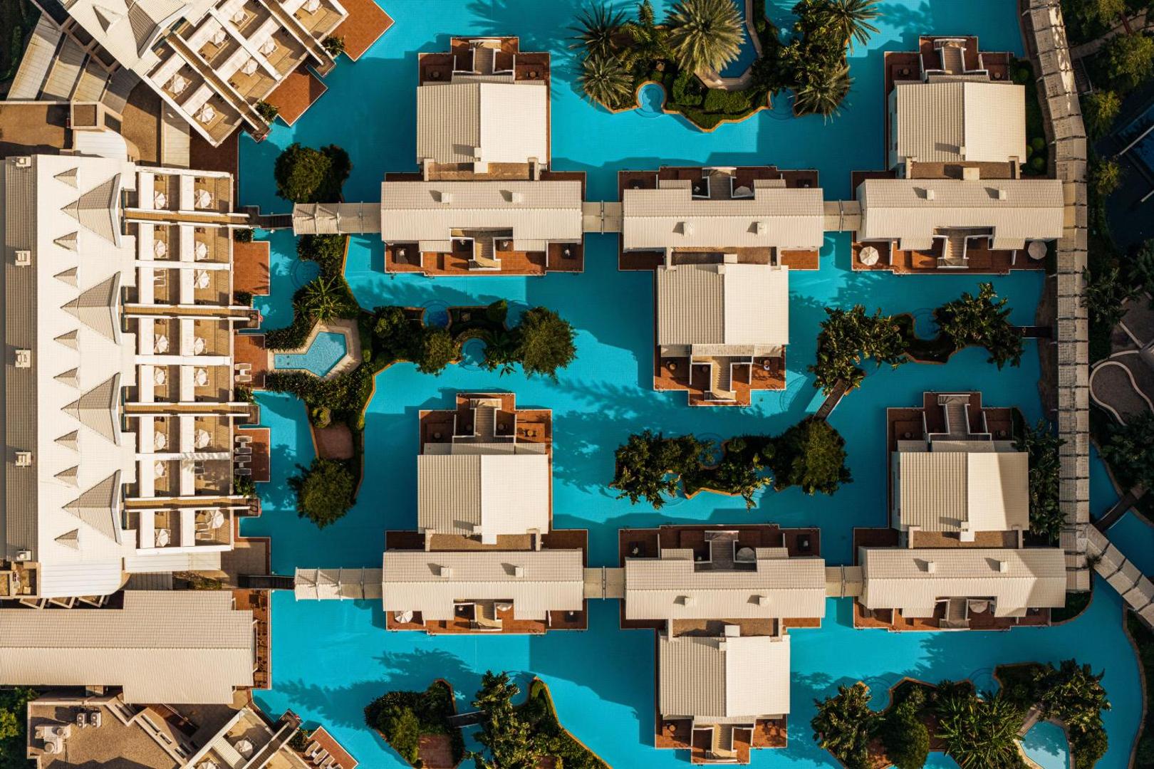 Susesi Luxury Resort skats no augšas uz bungalo tipa numuriem, kurus ieskauj zils baseins un zaļojošas palmas Belekā, Turcijā