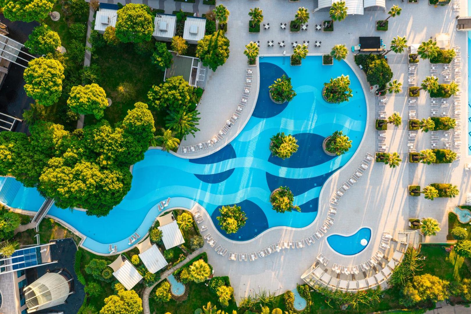 Susesi Luxury Resort galvenais baseins ar palmu salām un atpūtas krēsliem, uzņemts no putna lidojuma saulainā dienā