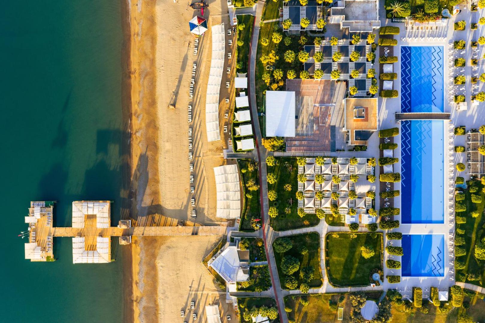 Susesi Luxury Resort Belekā no putna lidojuma — plaša teritorija ar baseiniem, dārziem un privāto pludmali ar koka piestātni