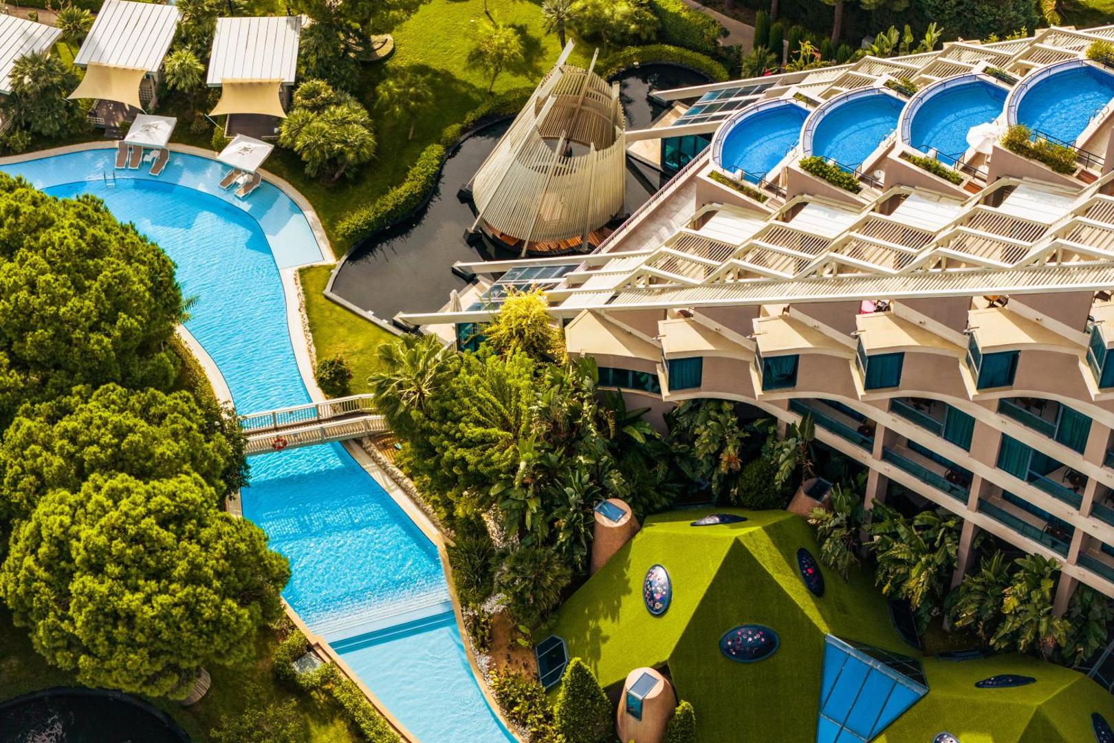 Susesi Luxury Resort arhitektūra un baseinu komplekss no putna lidojuma Belekā — kaskādes baseini, tiltiņi un zaļojoša teritorija