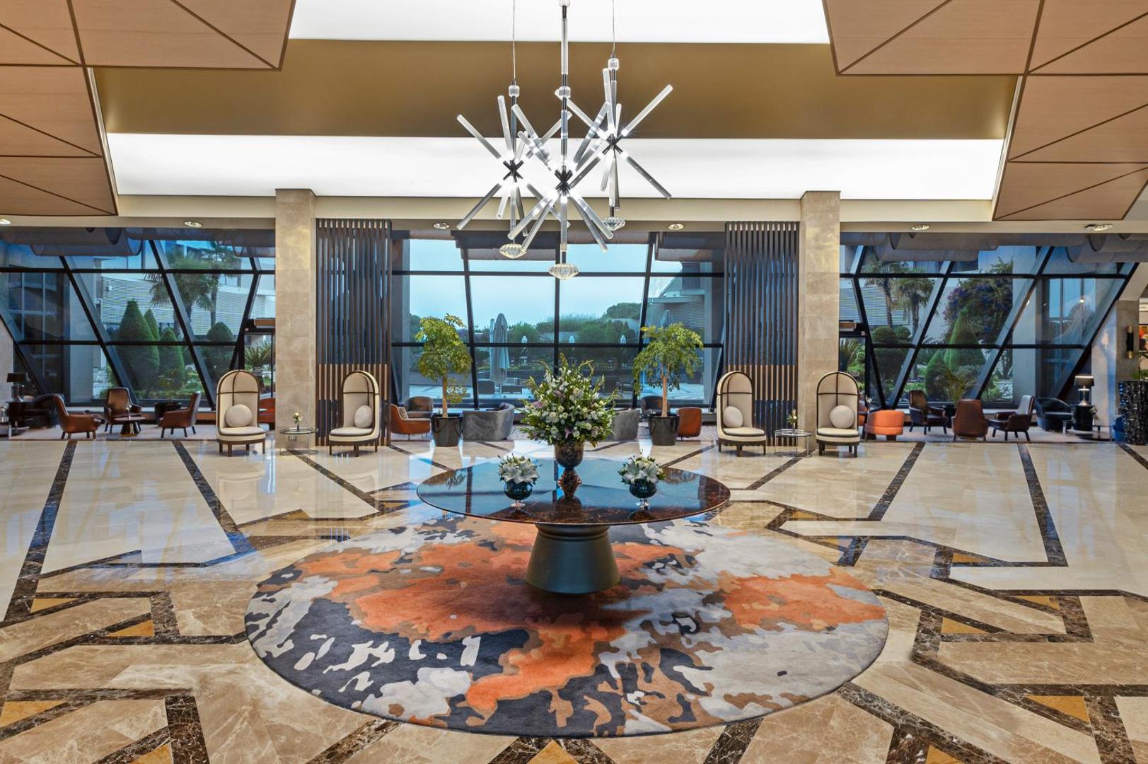 Susesi Luxury Resort greznais vestibils ar modernu lustru, marmora grīdu, dizaina mēbelēm un lieliem logiem uz dārzu