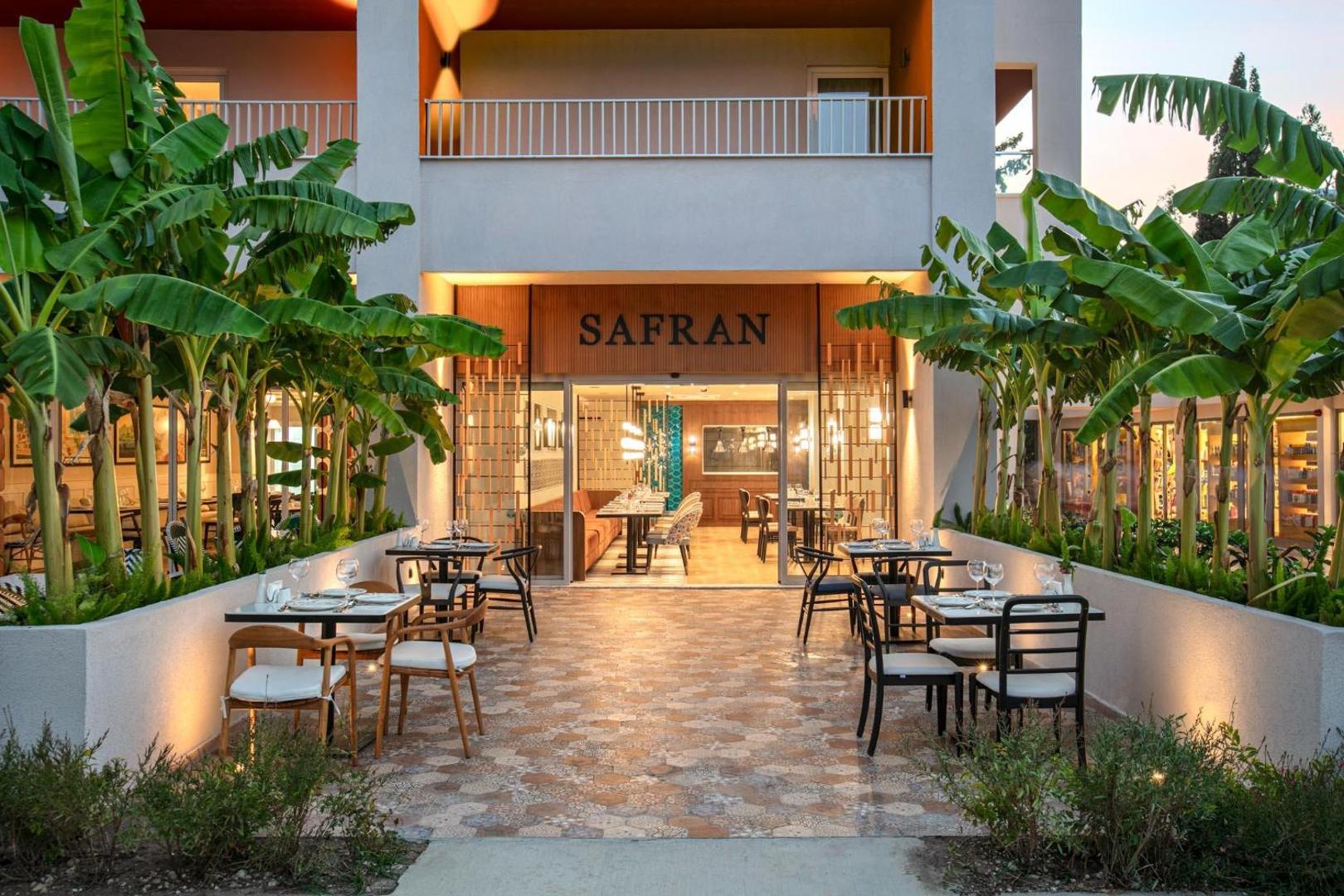 Greenwood Kemer Resort a la carte restorāns Safran vakarā — āra terase ar galdiņiem, banānu kokiem un siltu apgaismojumu Kemeras reģionā