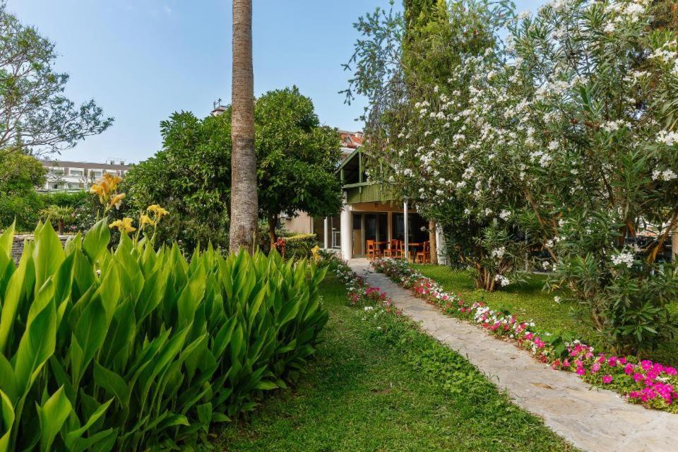 Greenwood Kemer Resort dārza celiņš ar ziedošām puķēm un palmām, kas ved uz mājīgu āra atpūtas zonu.