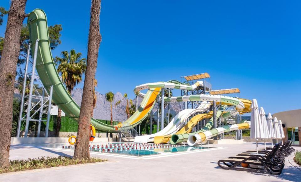 Greenwood Kemer Resort akvaparks ar vairākiem krāsainiem ūdens slidkalniņiem un palmām uz kalnu fona Kemeras kūrortā