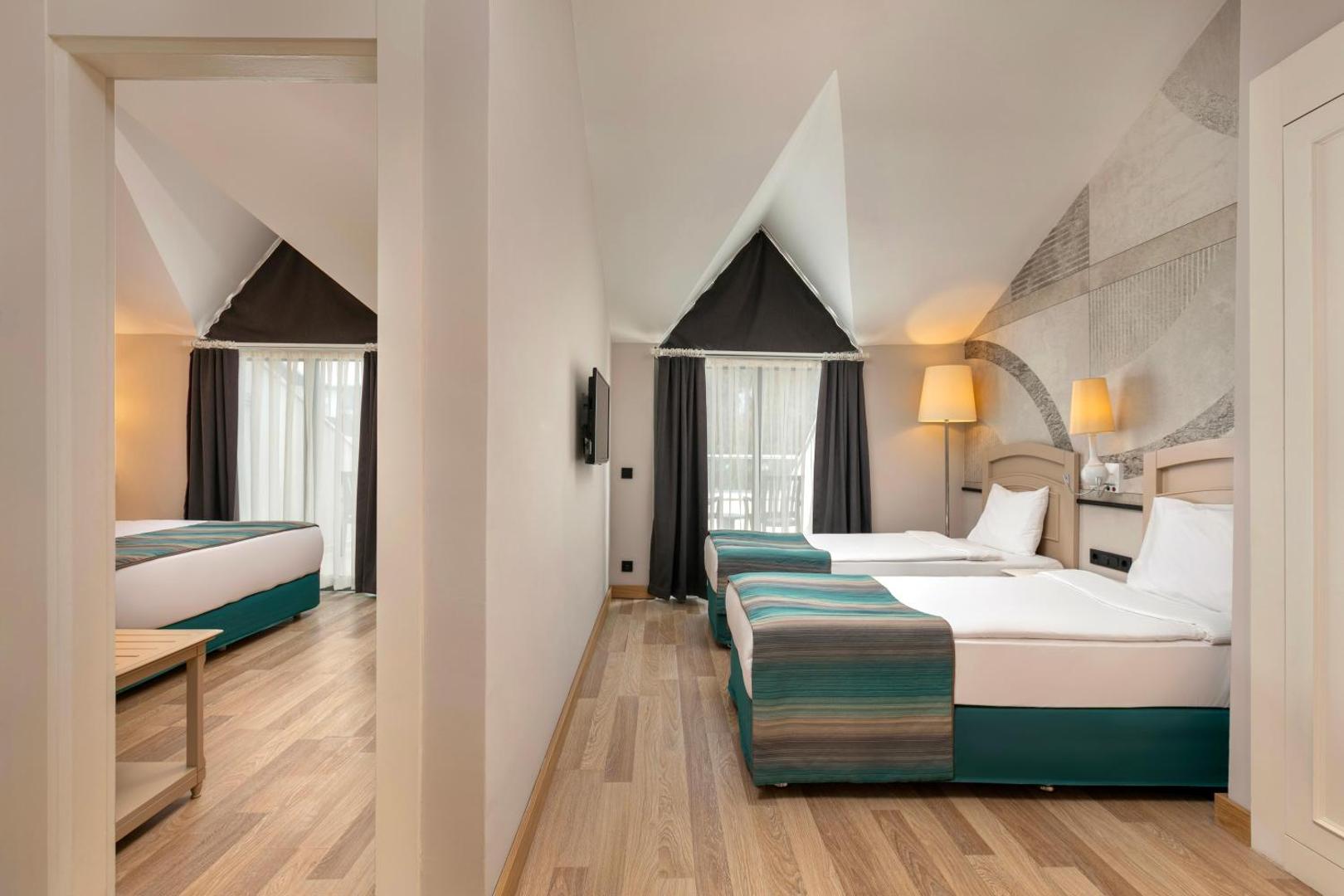 Greenwood Kemer Resort divstāvu ģimenes numurs ar atsevišķām guļamzonām, gaišu koka grīdu un modernu interjeru Kemeras reģionā, Turcijā.