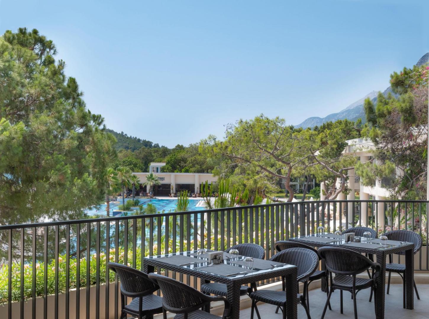 Skats no Sherwood Exclusive Kemer viesnīcas balkona uz plašo baseinu, zaļojošu dārzu un kalnu grēdu fonā Kemeras reģionā.