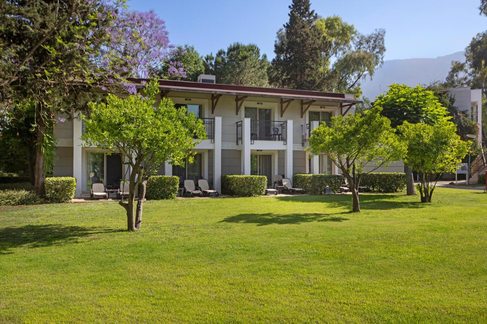 Sherwood Exclusive Kemer divstāvu bungalo tipa ēka ar balkoniem, ko ieskauj kopti mauriņi un ziedoši koki