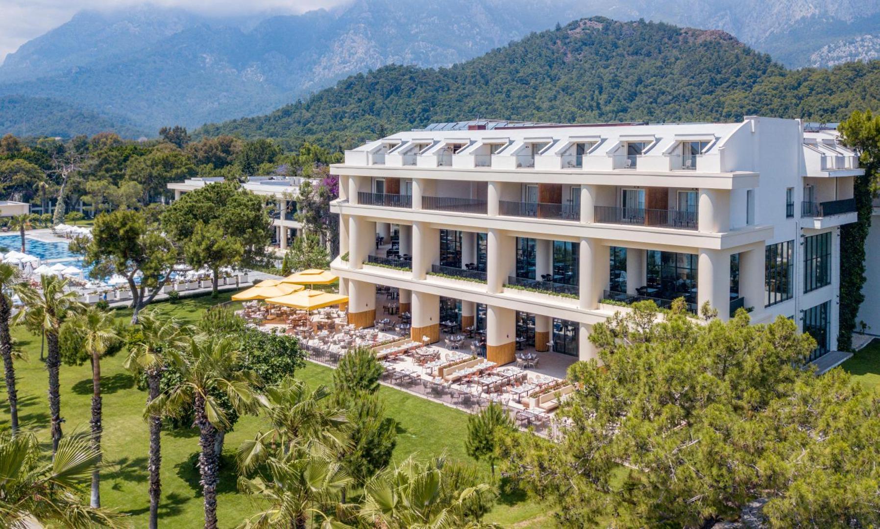Sherwood Exclusive Kemer galvenā ēka ar āra restorāna terasi, saulessargiem un palmām zaļā teritorijā