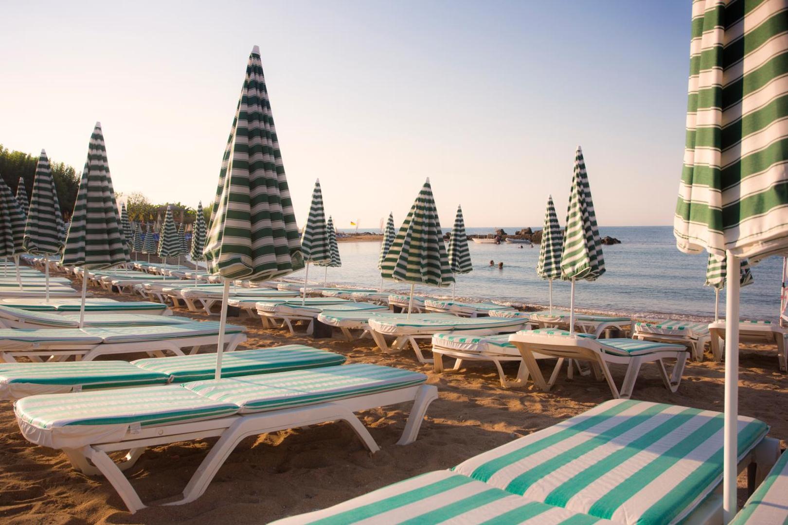 Lonicera Resort & Spa Hotel pludmales zona ar svītrainiem saulessargiem un ērtiem sauļošanās krēsliem smiltīs pie jūras