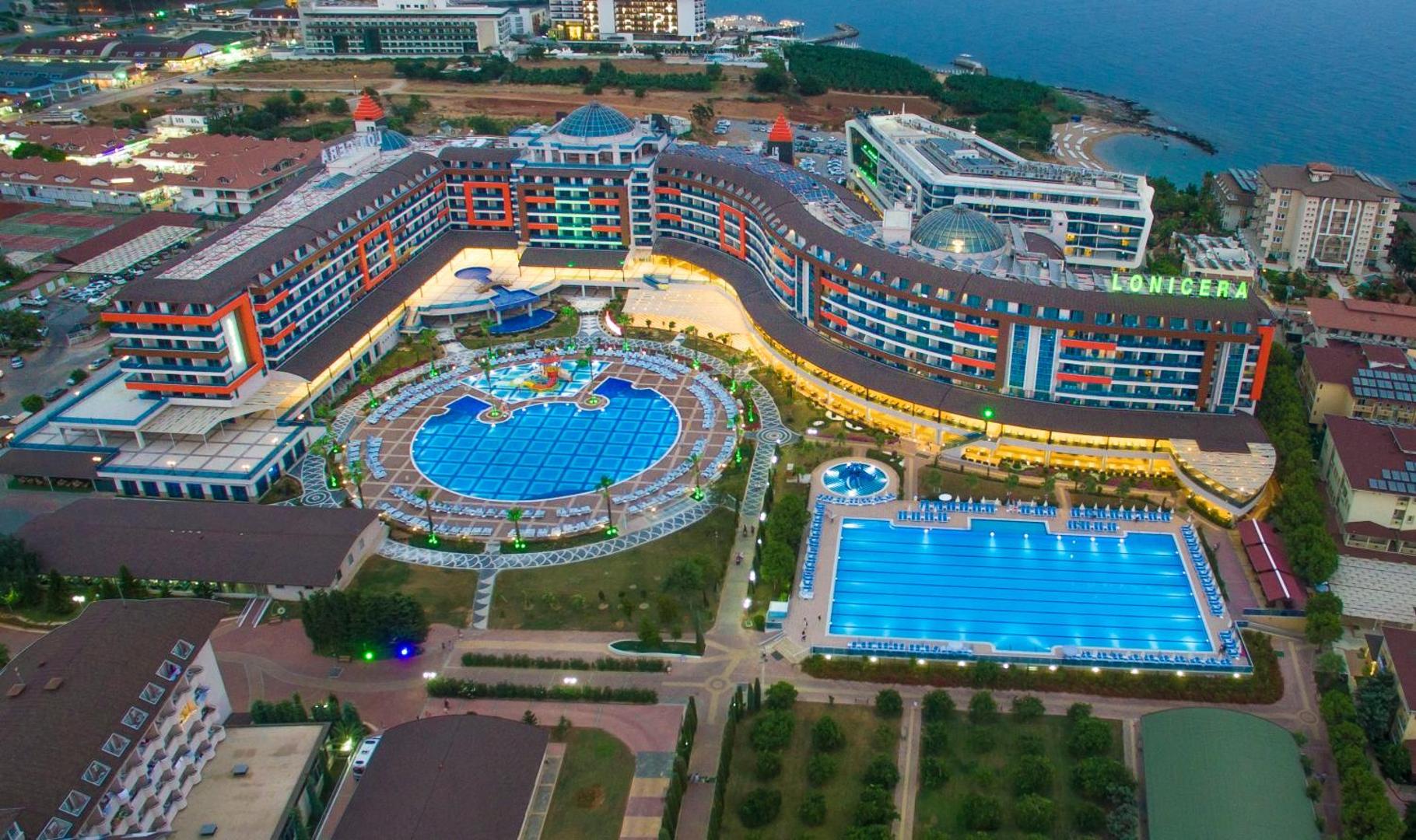 Lonicera Resort & Spa Hotel vakara skats no putna lidojuma uz izgaismotiem baseiniem un viesnīcas korpusiem Alanjas piekrastē