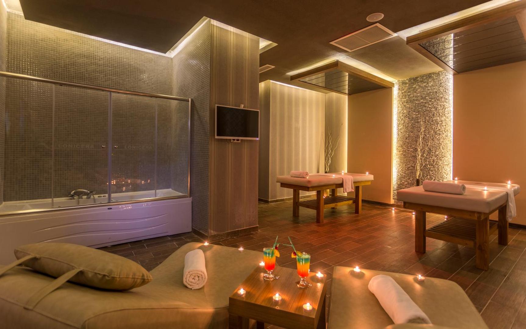 Lonicera Resort & Spa spa centrs Alanjā ar masāžas galdiem, džakuzi un atpūtas krēsliem sveču gaismā romantiskai atmosfērai