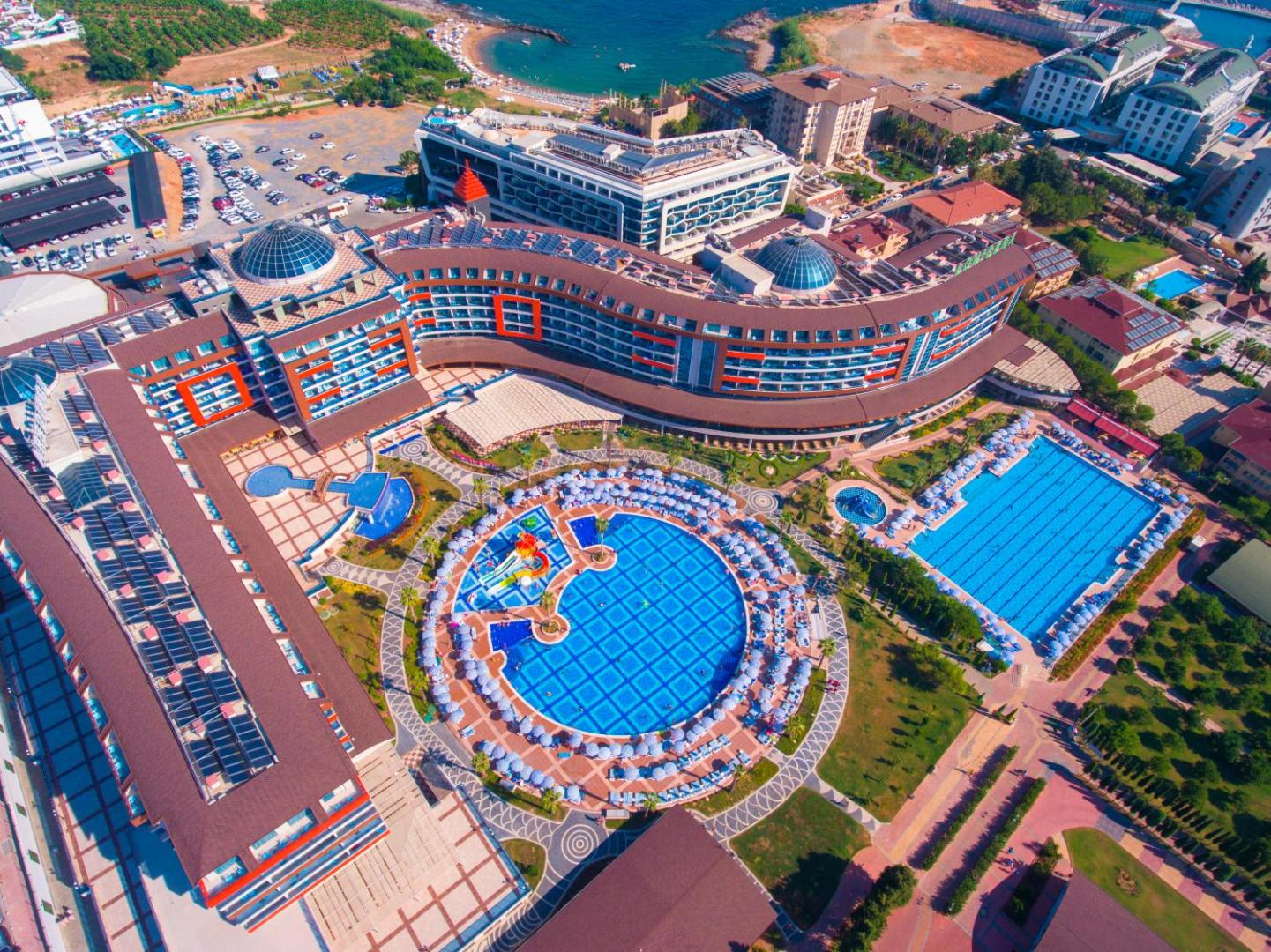 Lonicera Resort & Spa panorāmas skats dienā — lieli apaļi un taisnstūra baseini ar sauļošanās krēsliem pie jūras līča