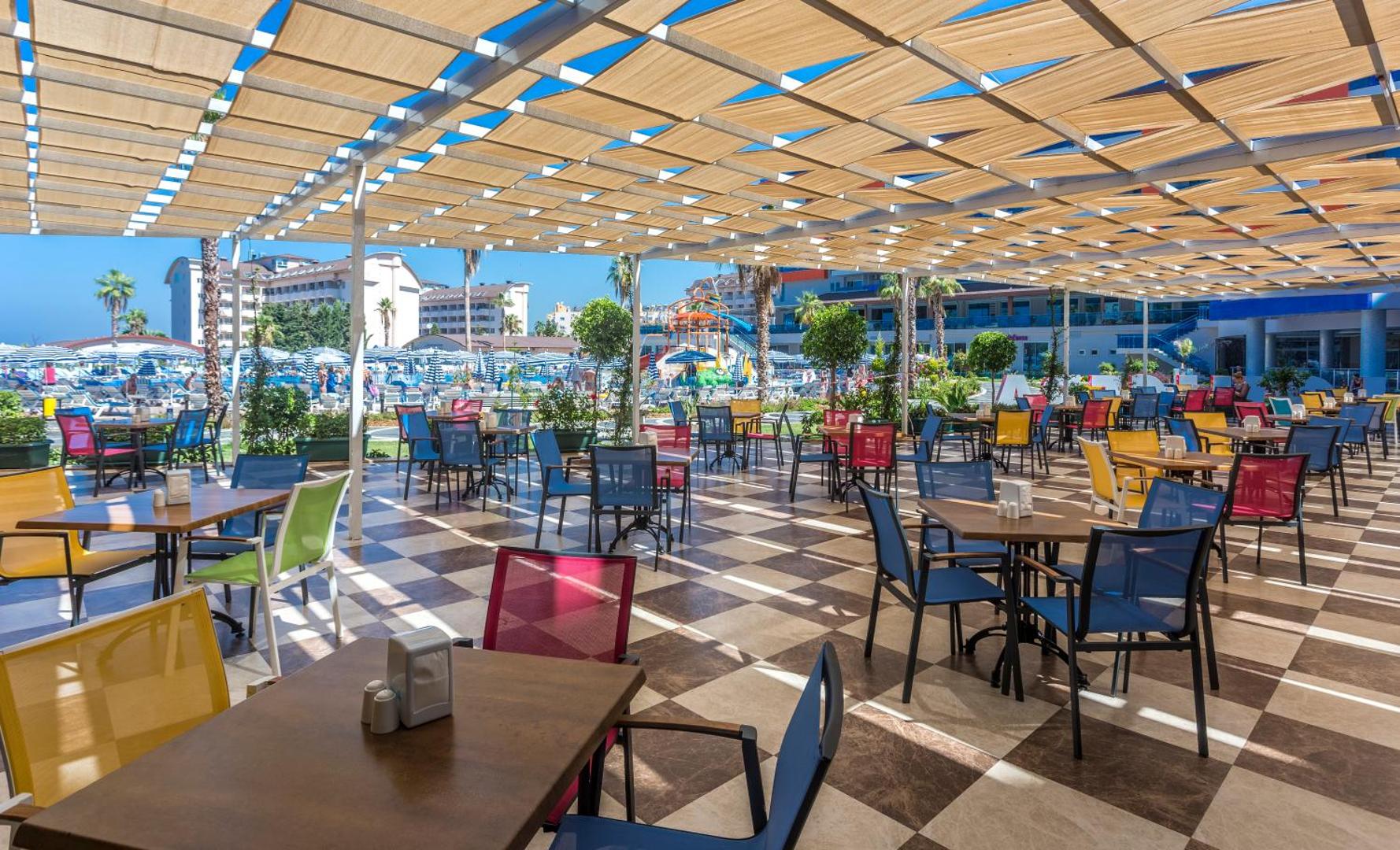 Lonicera Resort & Spa āra restorāna terase ar krāsainiem krēsliem zem nojumes un skatu uz viesnīcas teritoriju