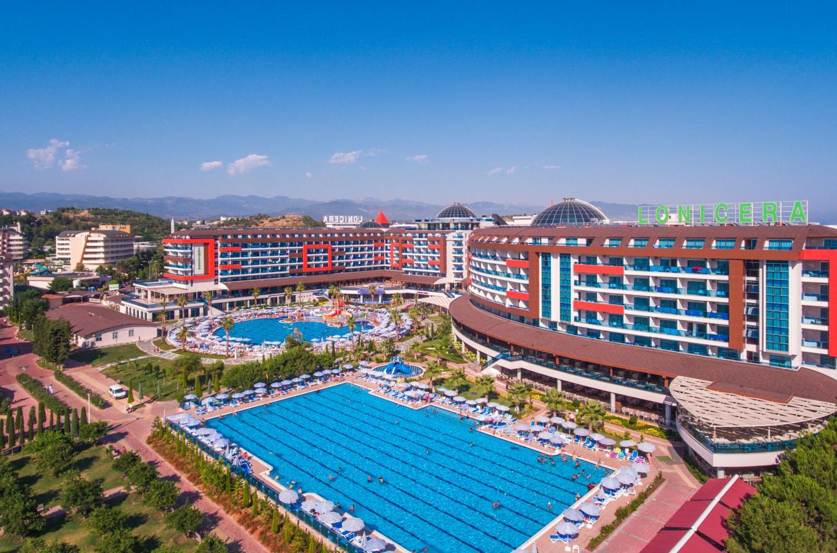Lonicera Resort & Spa Hotel panorāmas skats Alanjā ar plašiem āra baseiniem, viesnīcas korpusiem un saulessargu zonām piekrastē