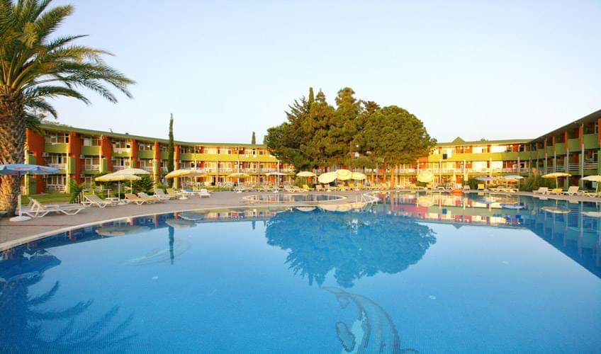 Lonicera Resort & Spa dārza korpuss ar āra baseinu, palmām un atpūtas krēsliem zaļā, labiekārtotā teritorijā