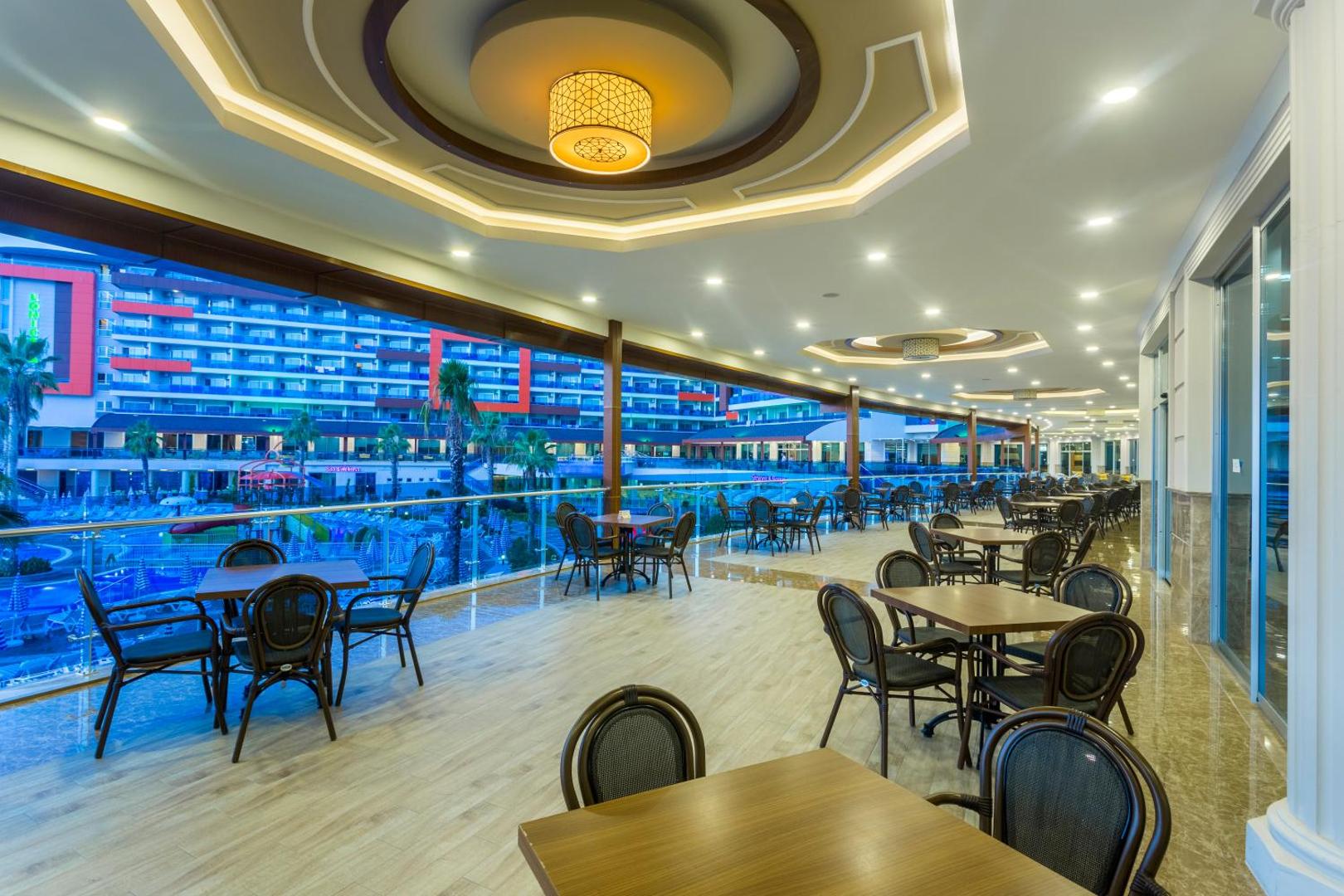 Lonicera Resort & Spa Hotel plašā āra terase ar galdiņiem un skatu uz kūrorta teritoriju un baseiniem vakara apgaismojumā