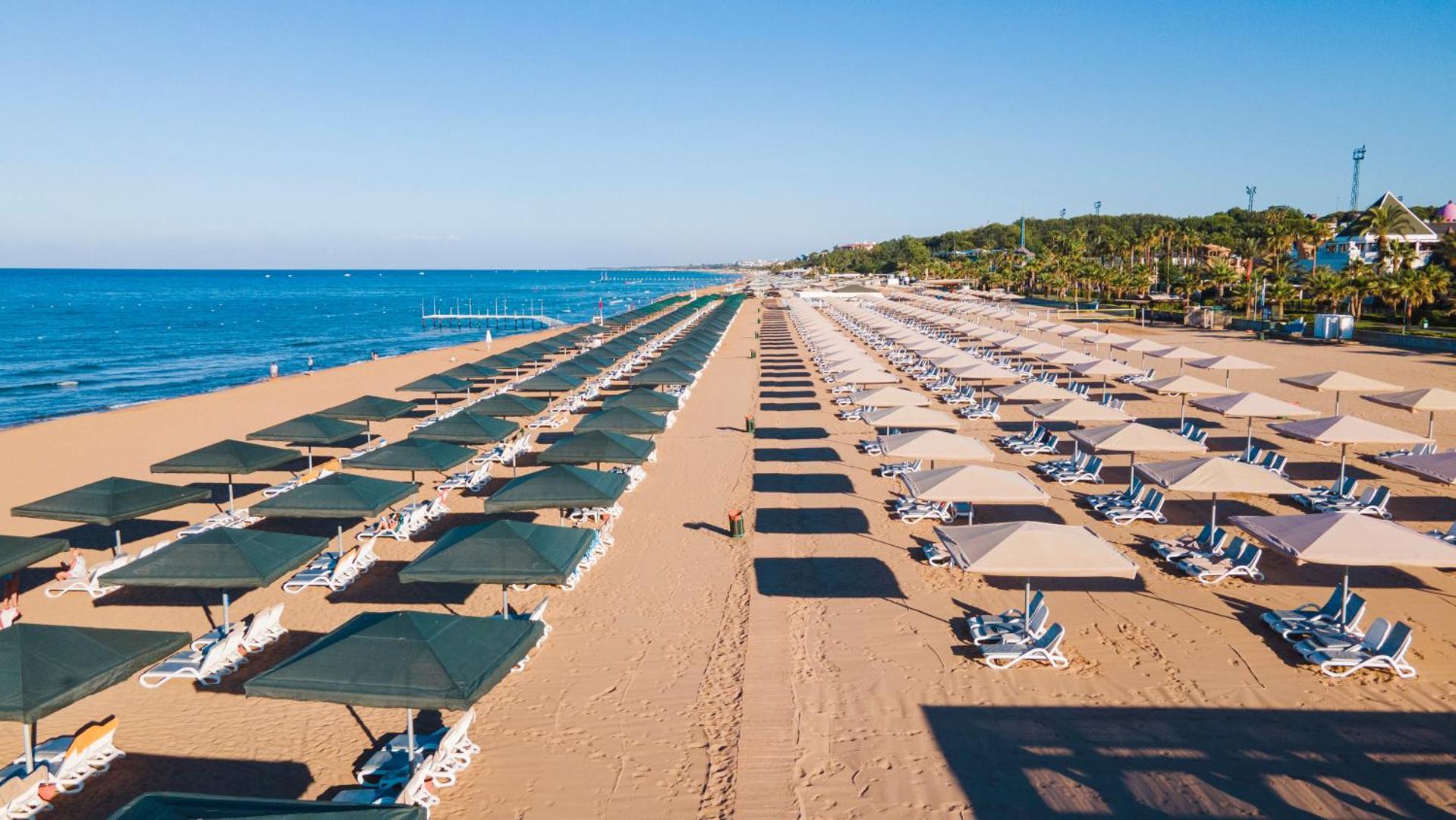 Sentido Kamelya Selin Luxury Resort & SPA privātā smilšu pludmale ar daudzām saulessargu rindām un sauļošanās krēsliem pie jūras.