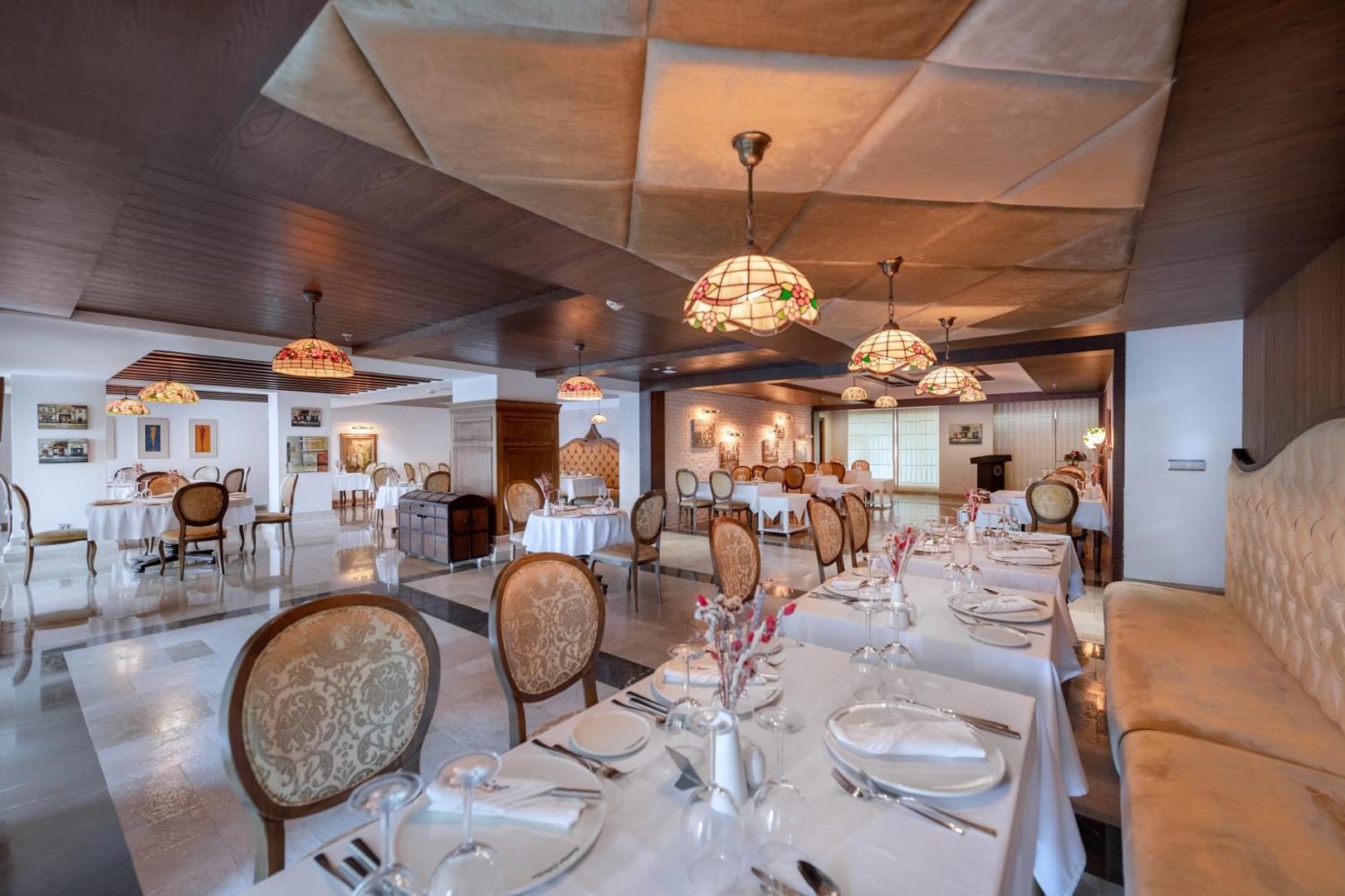 Sentido Kamelya Selin Luxury Resort & SPA restorāns ar eleganti klātiem galdiem, klasiskām mēbelēm un greznām lustrām Side, Turcijā.