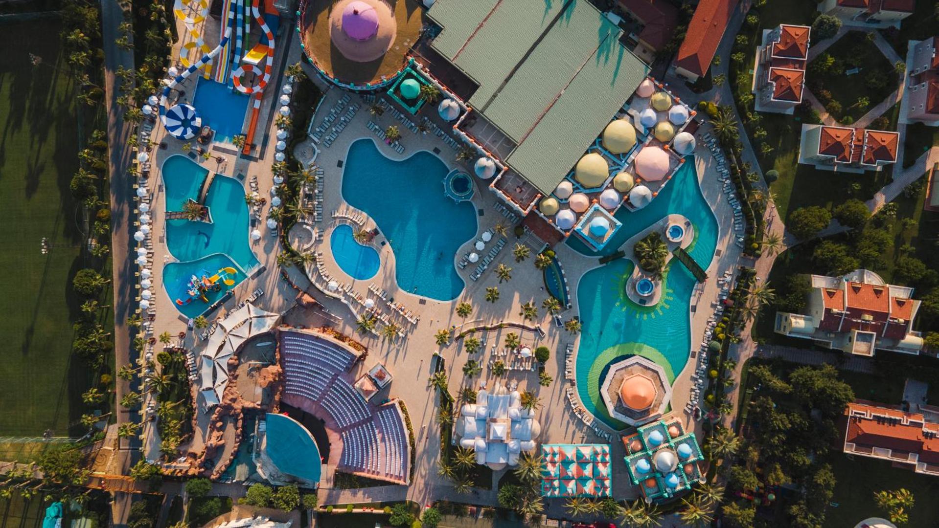 Sentido Kamelya Selin Luxury Resort & SPA teritorijas skats no augšas — baseinu komplekss, amfiteātris un atpūtas zonas palmu ieskāvumā