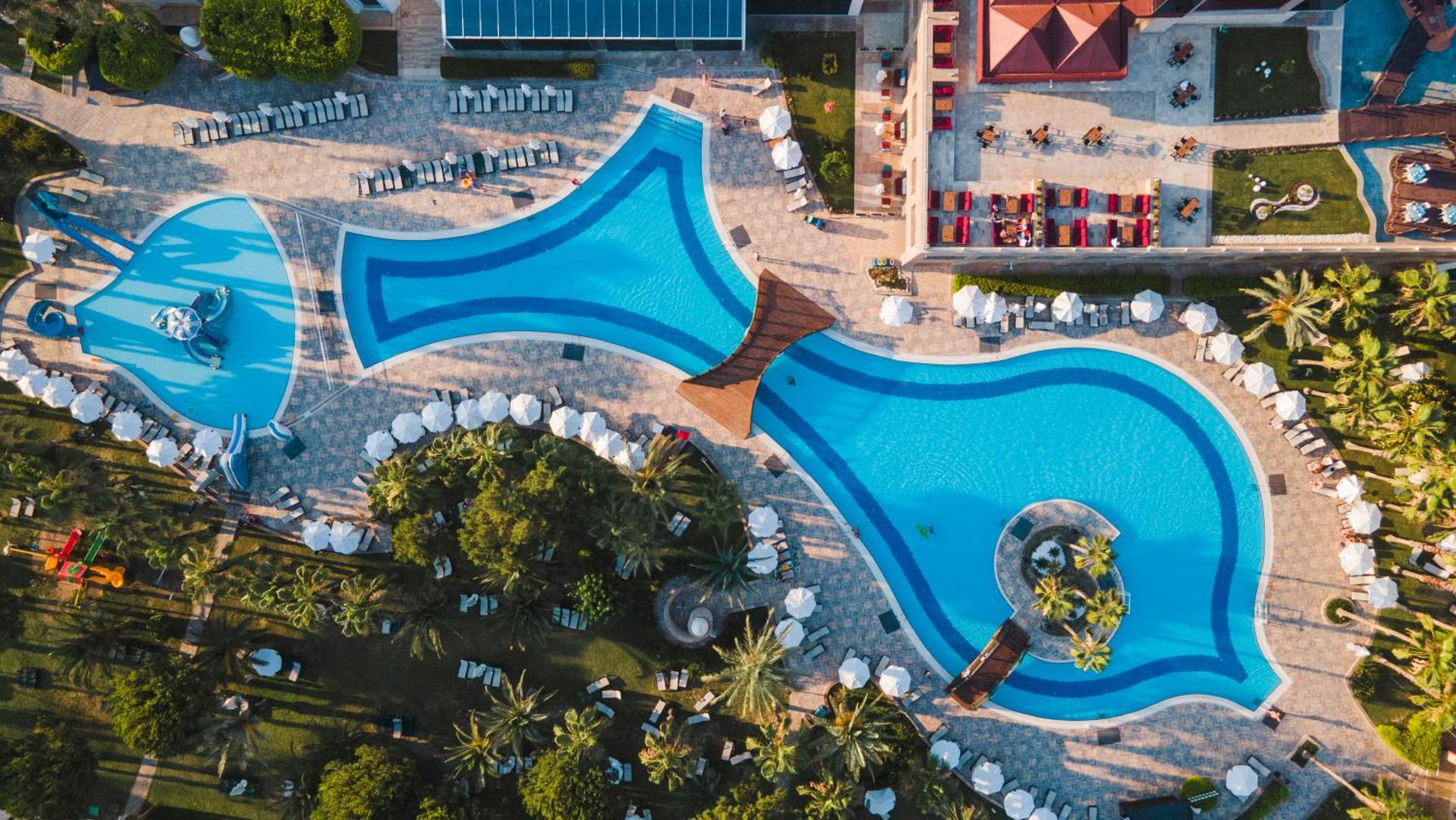 Sentido Kamelya Selin Luxury Resort & SPA plašie āra baseini no putna lidojuma Antaljas reģionā, Turcijā — atpūtas zona ar palmām un saulessargiem