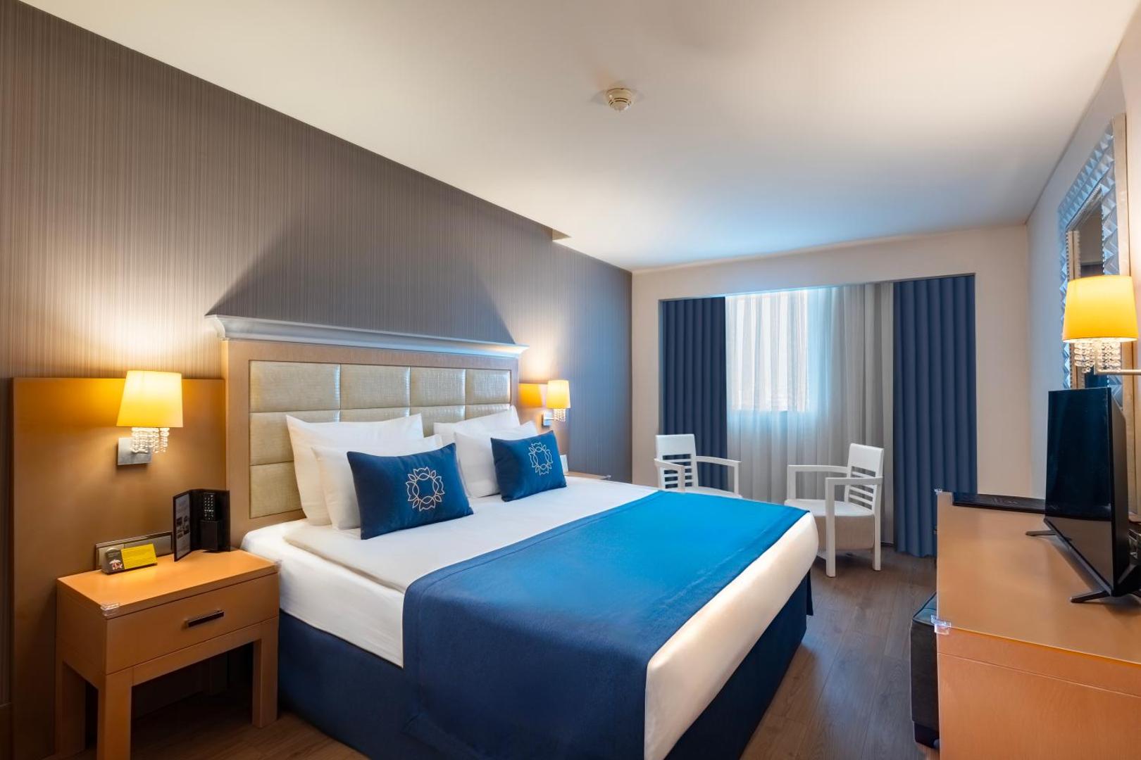 Sentido Kamelya Selin Luxury Resort & SPA moderns divvietīgs numurs ar ziliem akcentiem, lielu gultu un atpūtas zonu pie loga Sidē.