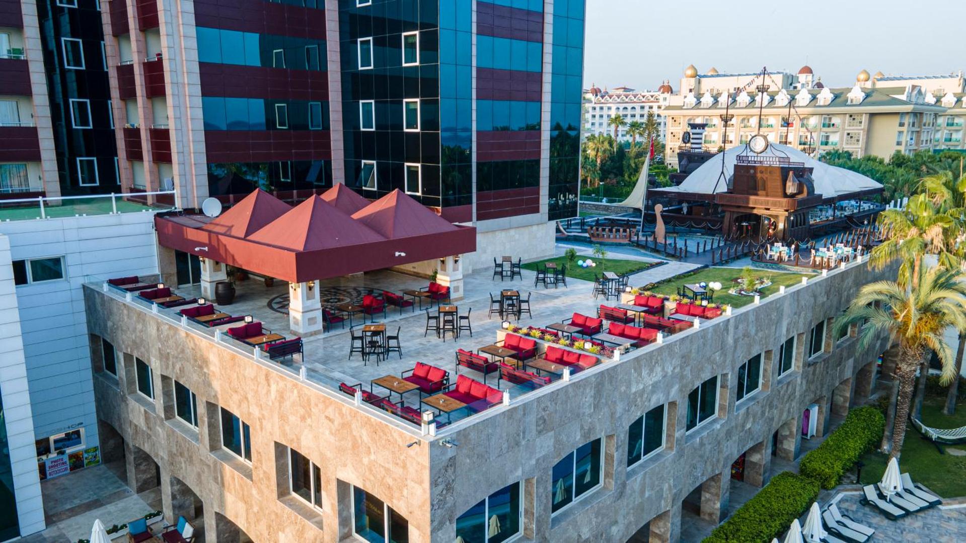 Sentido Kamelya Selin Luxury Resort & SPA āra terase ar atpūtas zonu, sarkaniem dīvāniem un skatu uz viesnīcas teritoriju.