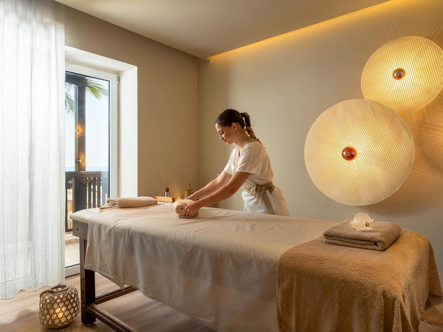 Grecotel Marine Palace & Aqua Park spa centra masāžas telpa ar siltu apgaismojumu un profesionālu aprīkojumu mierpilnai atpūtai Krētā