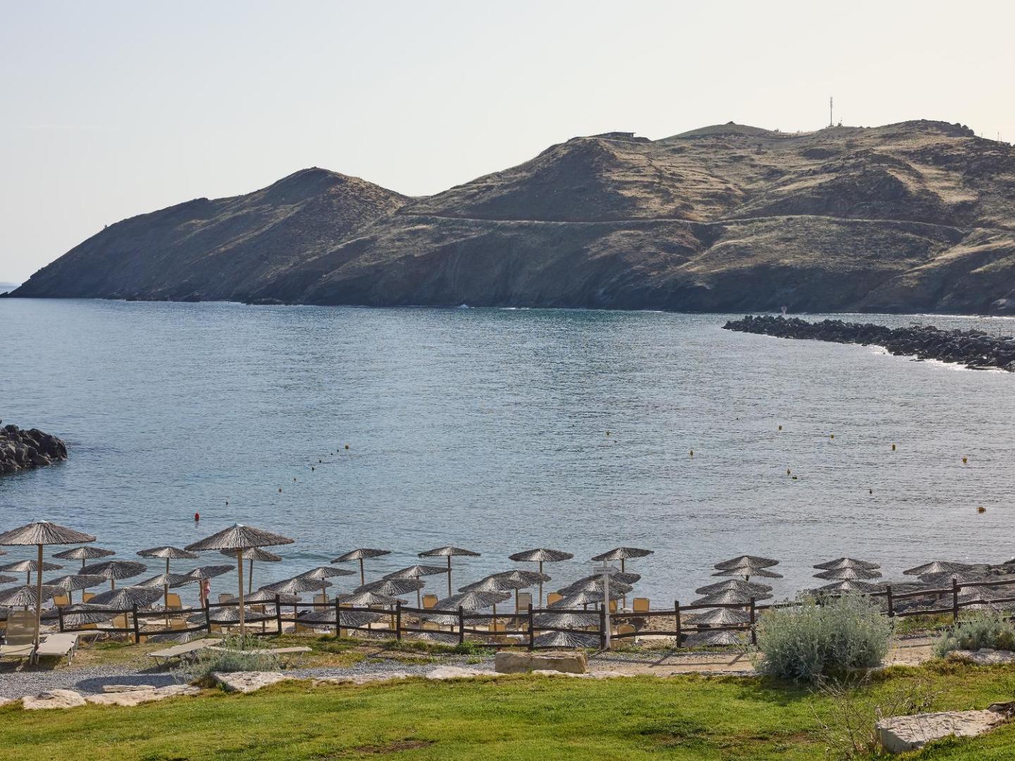 Grecotel Marine Palace & Aqua Park privātā pludmale līcī Panormo ciematā, Krētā — saulessargi un zviļņi pie mierīga, zila ūdens.