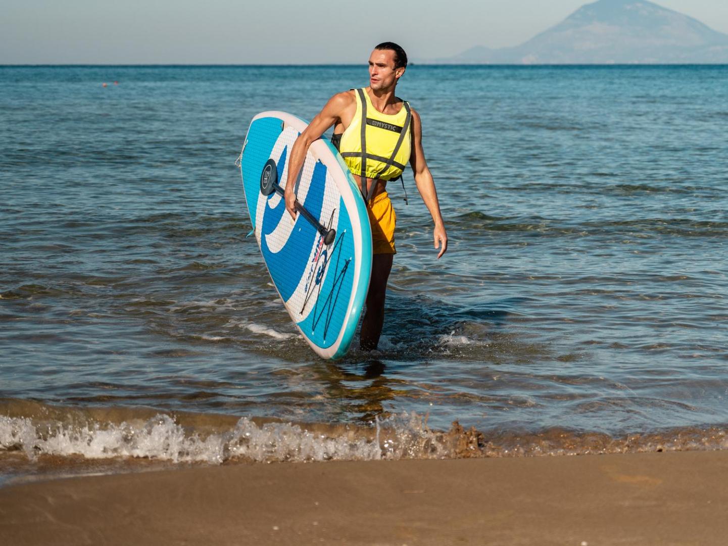 Vīrietis ar SUP dēli un glābšanas vesti iziet no jūras Grecotel Marine Palace & Aqua Park kūrortā Krētā.