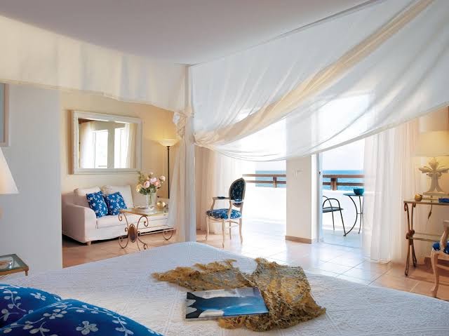 Grecotel Marine Palace & Aqua Park elegants suite numurs ar baldahīnu, viesistabas zonu un balkonu ar skatu uz jūru