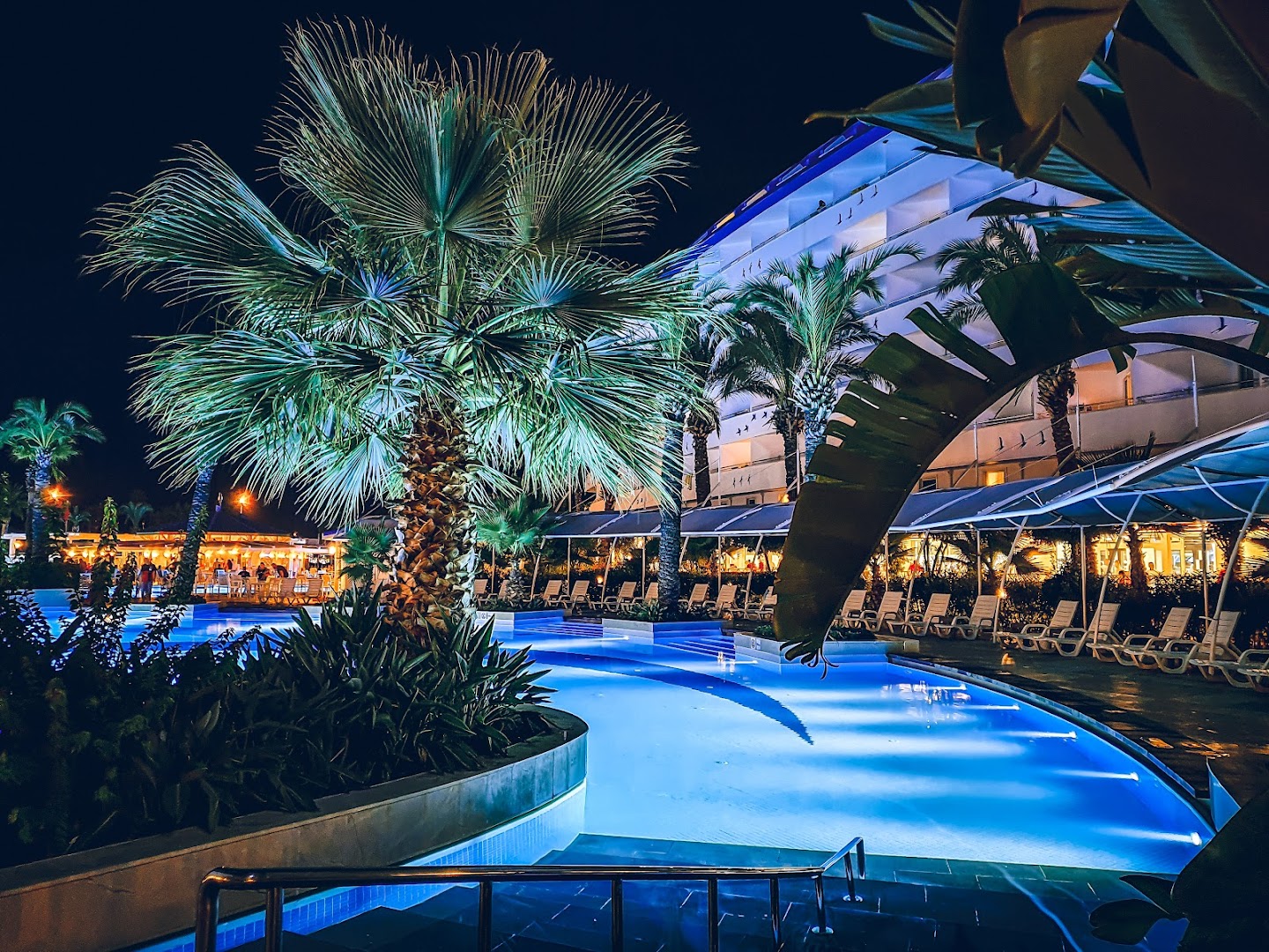 Crystal Admiral Resort Suites & Spa izgaismots āra baseins nakts laikā ar palmām un viesnīcas korpusu fonā Sidē