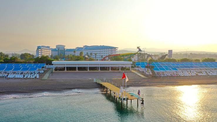 Crystal Admiral Resort Suites & Spa skats no putna lidojuma uz privāto pludmali, piestātni un viesnīcas ēku saulrietā Antalijā