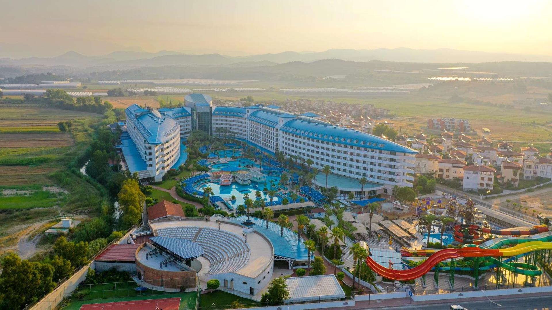 Crystal Admiral Resort Suites & Spa panorāmas skats saulrietā — plaša teritorija ar baseiniem, amfiteātri un akvaparku Sides reģionā, Turcijā