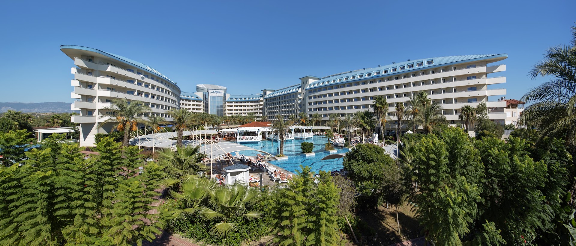 Crystal Admiral Resort Suites & Spa galvenais baseins un viesnīcas fasāde dienā — saulaina atpūtas zona ar sauļošanās krēsliem un palmām