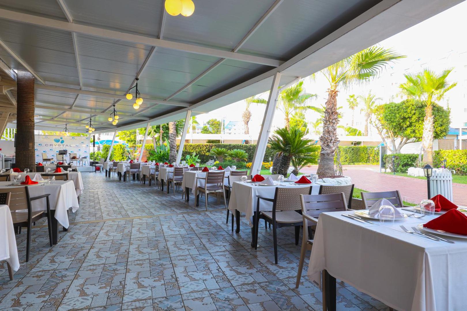 Crystal Admiral Resort Suites & Spa āra restorāna terase ar klātiem galdiem, palmām un skatu uz viesnīcas teritoriju