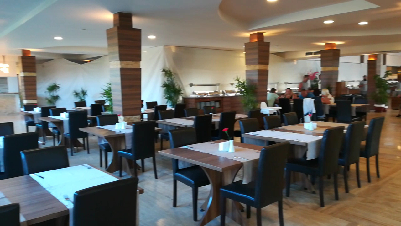 Club Turan Prince World galvenā restorāna iekštelpas ar koka kolonnām, galdiņiem un bufetes zonu gaišā, plašā telpā