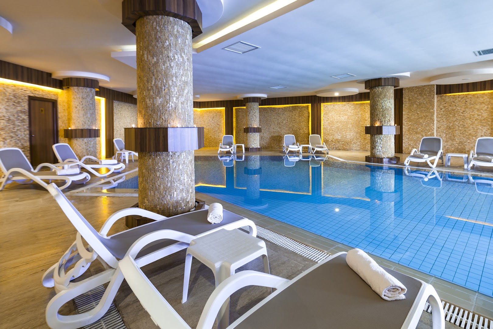 Club Turan Prince World iekštelpu baseins spa centrā ar apsildāmu ūdeni, sauļošanās krēsliem un dekoratīvām akmens kolonnām