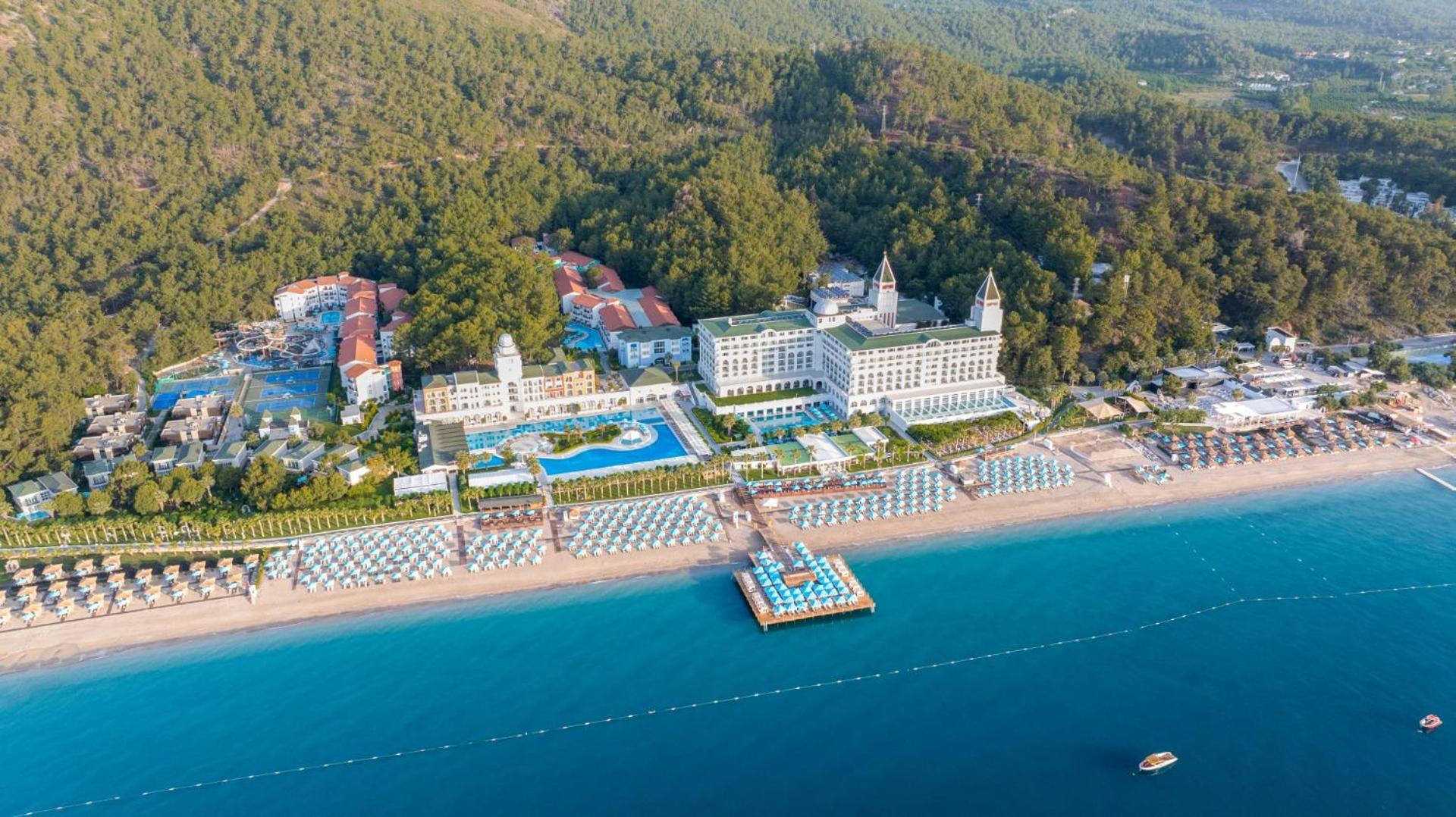 Nirvana Dolce Vita viesnīcas panorāmas skats no putna lidojuma — piekrastes līnija, privātā pludmale, baseini un priežu mežs fonā
