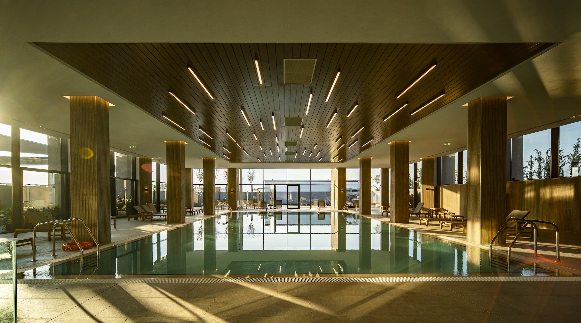 The Wave Resort moderns iekštelpu baseins ar koka apdari, panorāmas logiem un ērtiem atpūtas krēsliem spa zonā