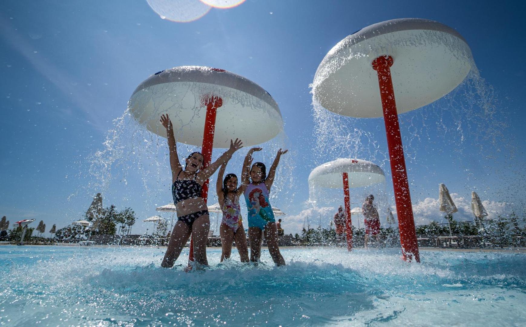 Bērni spēlējas The Wave Resort seklajā baseinā zem sēņu formas ūdens strūklakām saulainā dienā kūrorta bērnu zonā