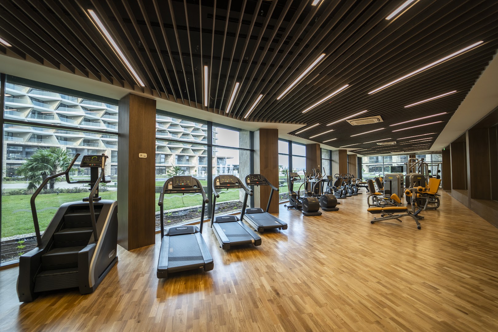 The Wave Resort modernais fitness centrs ar skrejceliņiem un trenažieriem, koka grīdu un skatu caur lieliem logiem uz viesnīcu