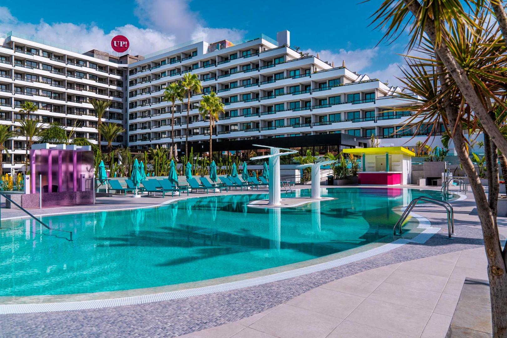 Viesnīcas Bitacora modernā ēka un lielais āra baseins ar ziliem saulessargiem un palmām Tenerifes kūrortā
