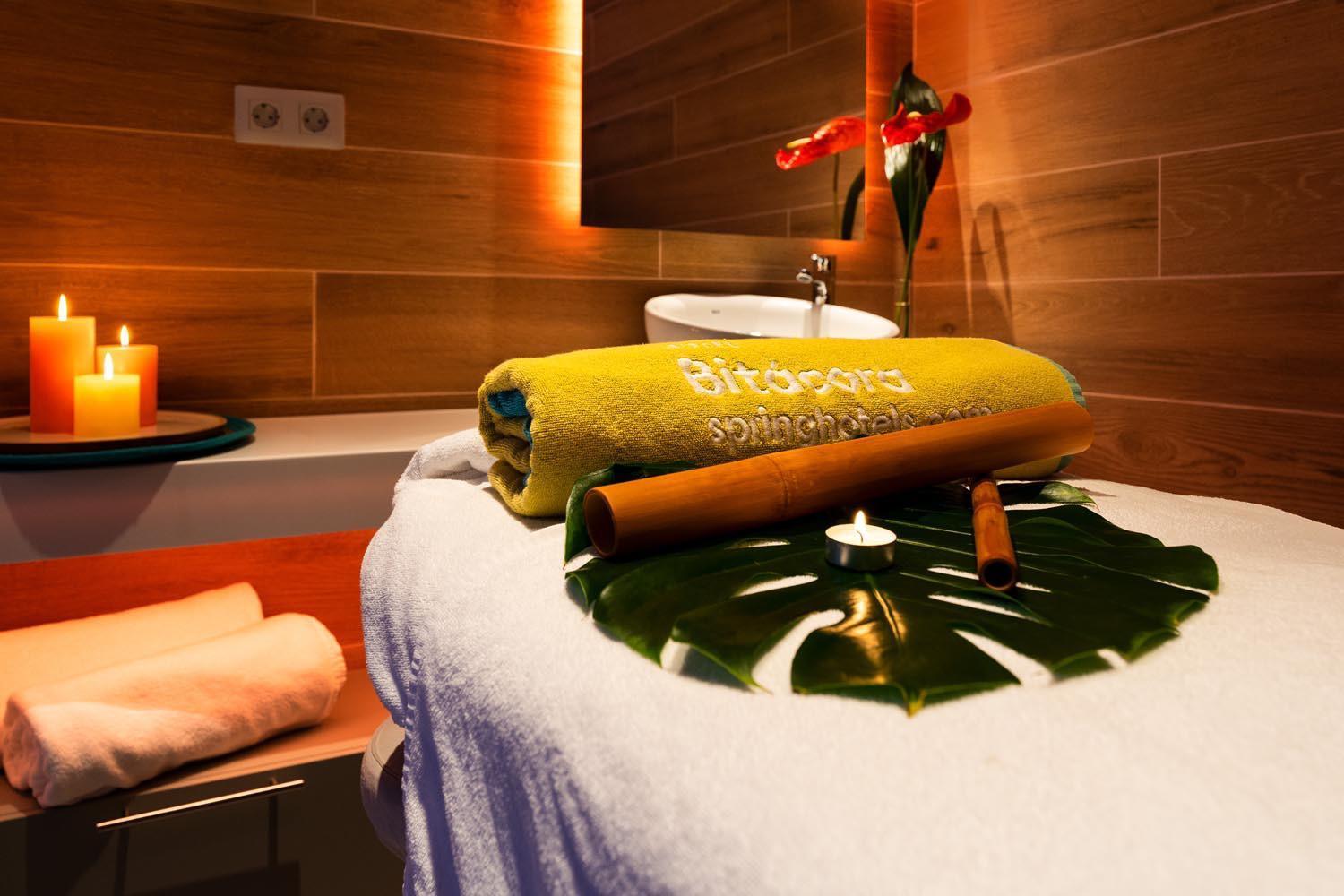 Tuvplāns ar masāžas galdu Hotel Bitacora spa centrā — dzeltenu dvieli, bambusa nūjiņām un dekoratīvām svecēm Tenerifē