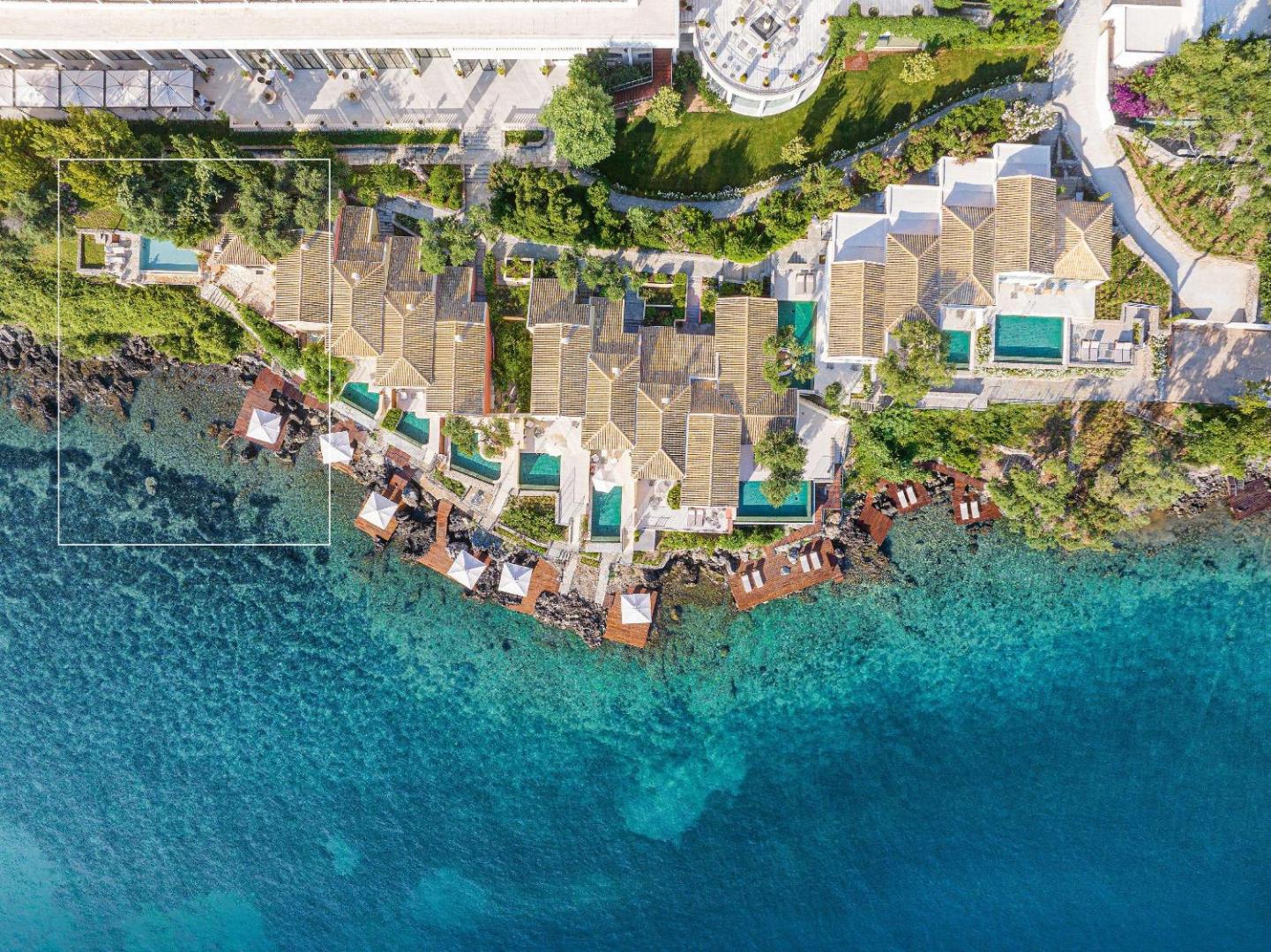 Corfu Imperial Grecotel Exclusive Resort villu komplekss no augšas ar privātiem baseiniem un koka sauļošanās platformām uz klintīm.