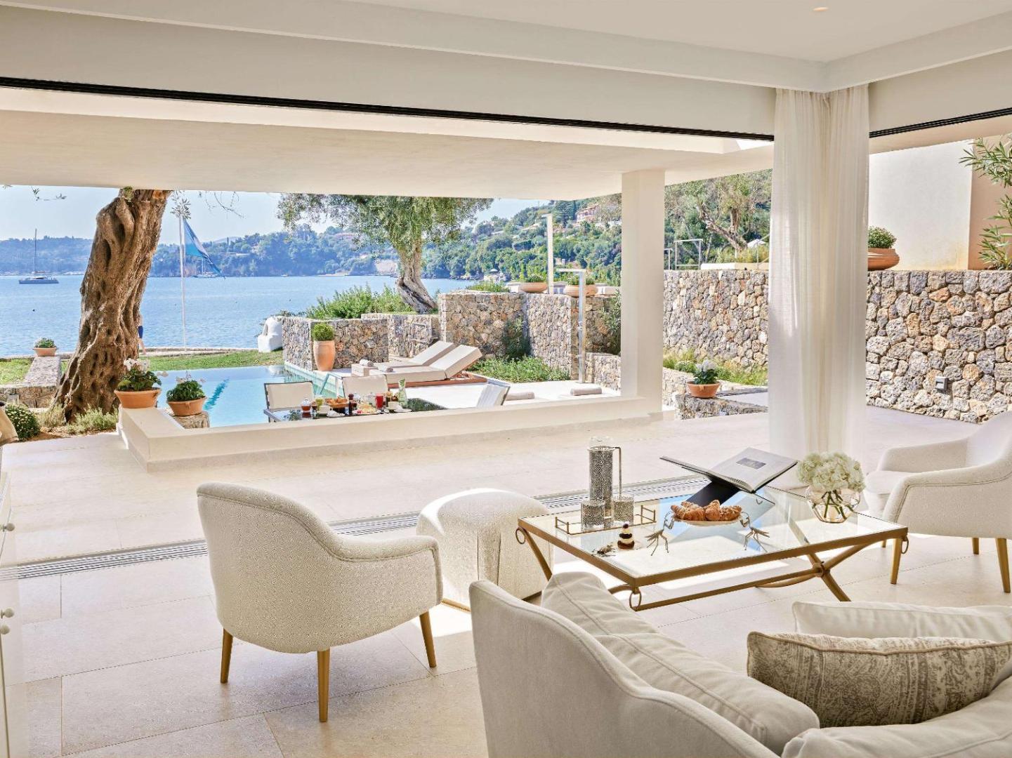Corfu Imperial Grecotel Exclusive Resort āra terase ar skatu uz jūru, baseinu un olīvkokiem, mīkstajiem krēsliem un brokastu galdu