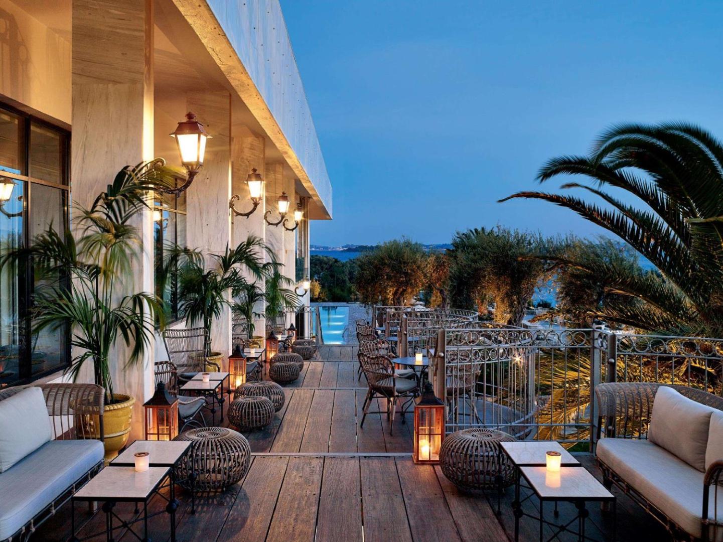 Corfu Imperial Grecotel Exclusive Resort āra terase vakarā ar mīkstajiem krēsliem, laternām un skatu uz Jonijas jūru Korfu salā