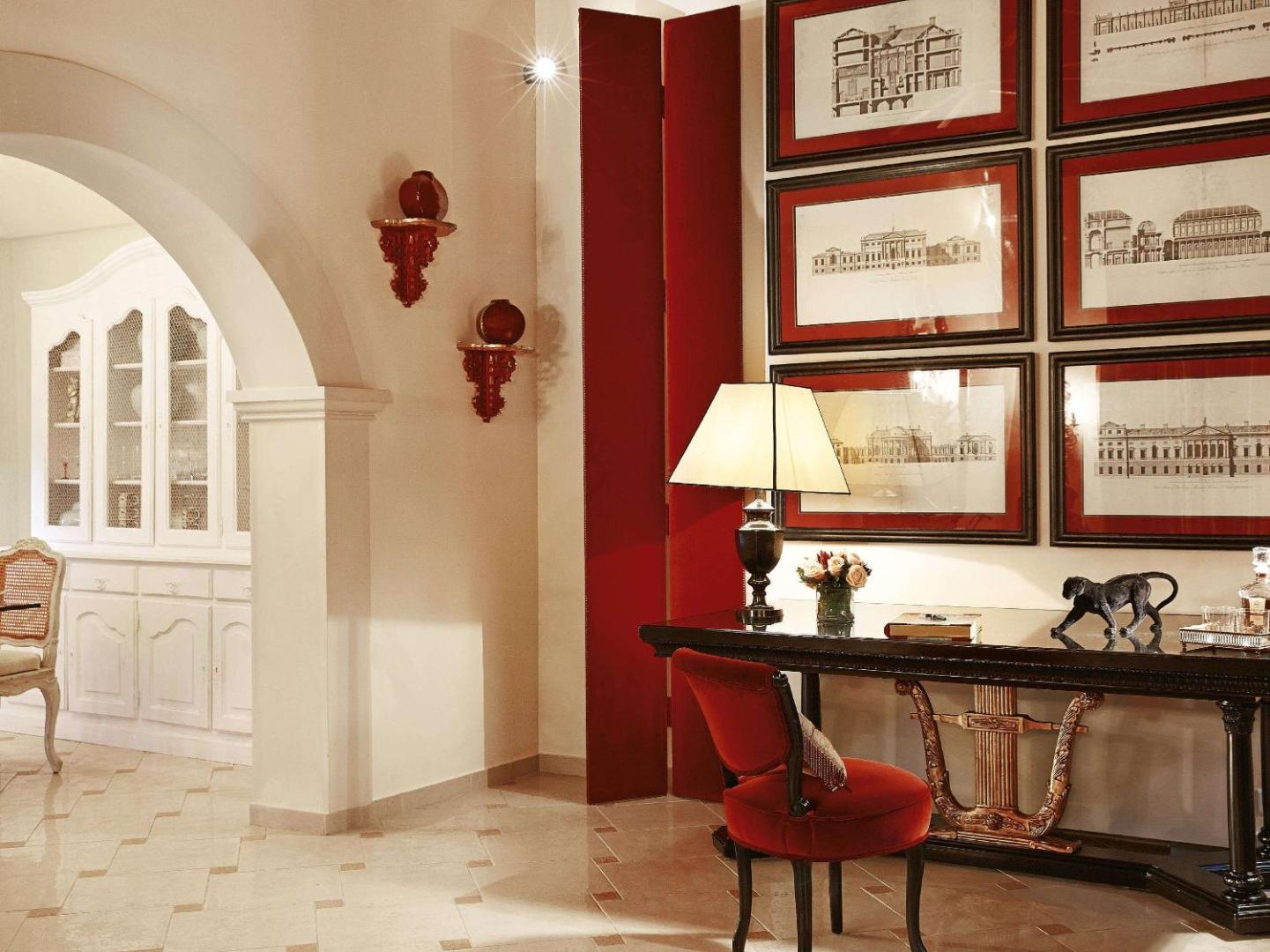 Corfu Imperial Grecotel elegants interjera stūris ar sarkaniem akcentiem, klasiskām gleznām pie sienas un antīka stila mēbelēm.