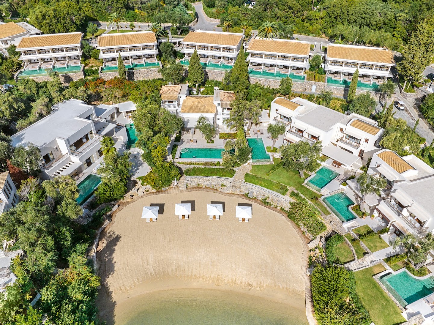 Corfu Imperial Grecotel Exclusive Resort terasveida numuri ar baseiniem un privātu, pusapaļu smilšu pludmali, ko ieskauj zaļumi.