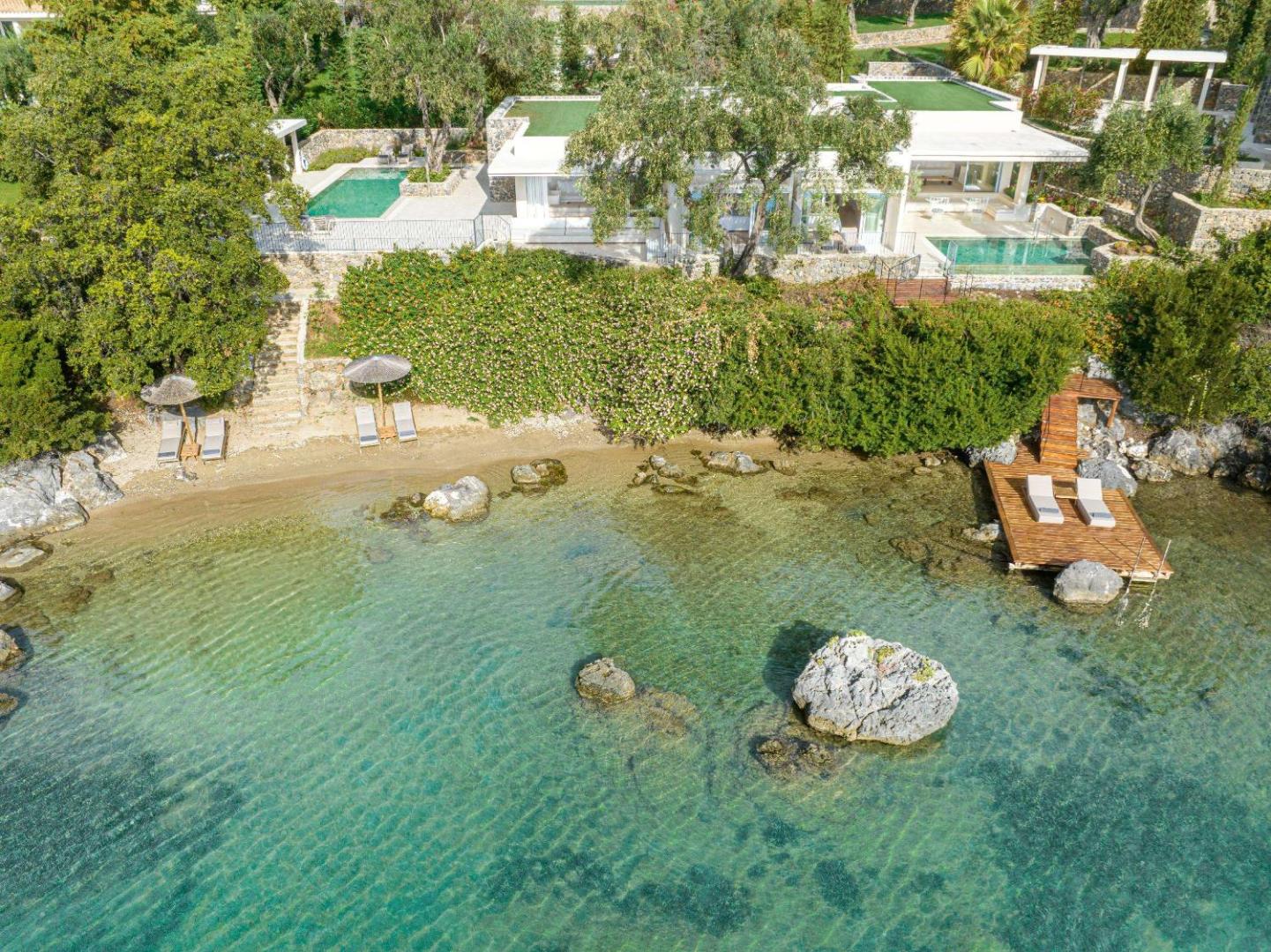 Corfu Imperial Grecotel Exclusive Resort moderna villa ar baseinu un tiešu piekļuvi nelielai, smilšainai pludmalei un koka laipai.